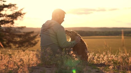 Loving man strokes cocker spaniel dog sitting in field grass at back sunset man enjoys rest with...