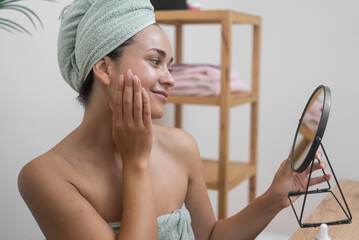 A lady gazes into a table's round mirror, caressing her velvety skin during a pampering day of...