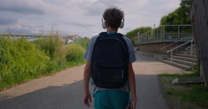 A teenager guy on the background of a beautiful old city in headphones travels around the city and listens to music. View from the back