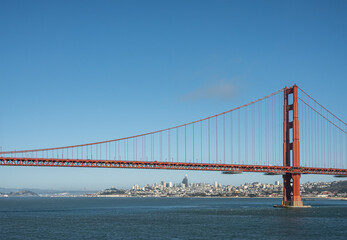 San Francisco, CA, USA - July 13, 2023: Approaching downtown urban jungle, seen from ocean side Golden Gate bridge, with 1 tower, under blue sky, behind blue bay water