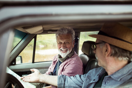 Happy gay senior couple driving a car and navigating with a map while going on a road trip to camp and hike - Powered by Adobe