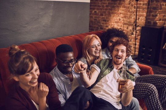 Young and diverse group of friends having fun and drinking beer on the couch at a house party