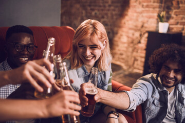 Young and diverse group of friends having a beer during a house party on the couch