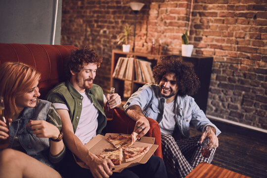 Young and diverse group of friends having a beer and pizza party at home on the couch