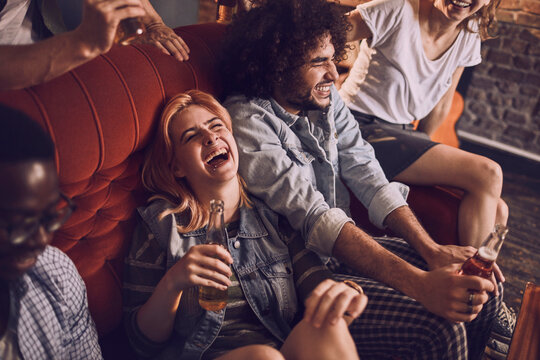 Young and diverse group of friends having a beer during a house party on the couch