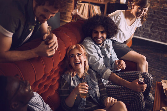 Young and diverse group of friends having a beer during a house party on the couch