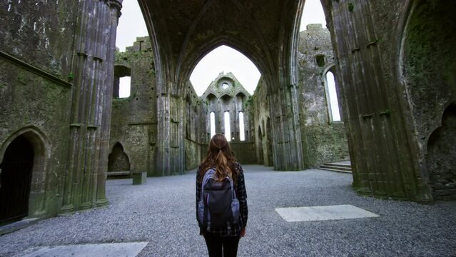 Woman standing in ruins of cathedral alone as camera pushes back revealing location. Rock of Cashel