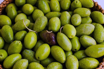 Freshly harvested green natural olives in wicker basket on white surface