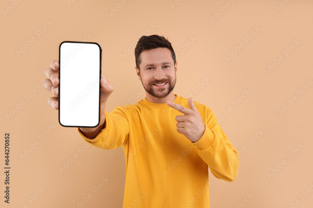 Poster handsome man showing smartphone in hand and pointing at it on light brown background