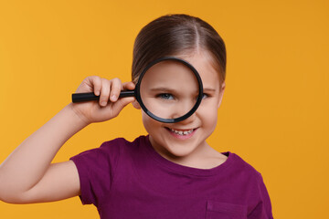 Cute little girl looking through magnifier on orange background