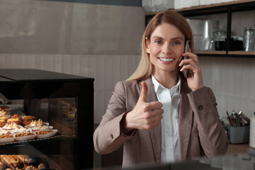 Happy business owner talking on phone and showing thumb up in bakery shop
