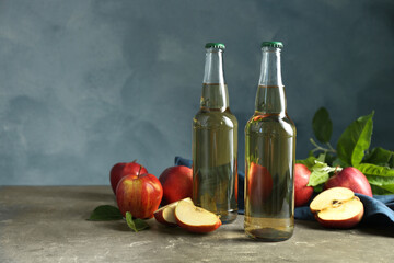 Delicious cider and apples with green leaves on gray table