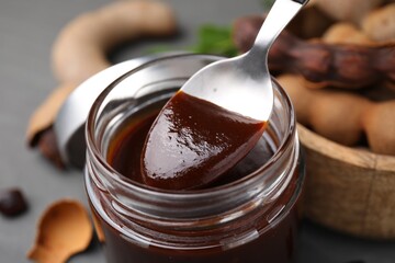 Taking tasty tamarind sauce with spoon from jar on table, closeup - obrazy, fototapety, plakaty