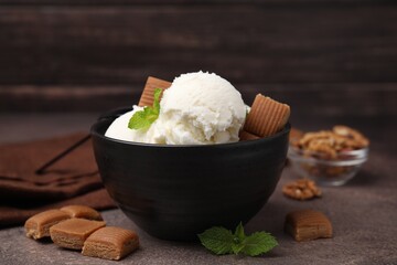 Tasty ice cream with caramel candies and mint in bowl on brown table, closeup