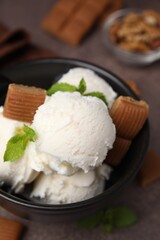 Tasty ice cream with caramel candies and mint in bowl on brown table, closeup