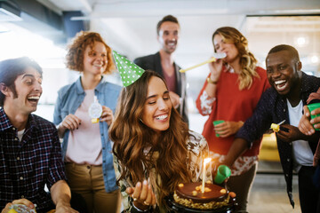 Young and diverse group of people celebrating a surprise birthday party in the office of a startup...
