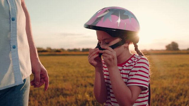 Preschooler girl fastens clasp on helmet strap for bicycle riding with father
