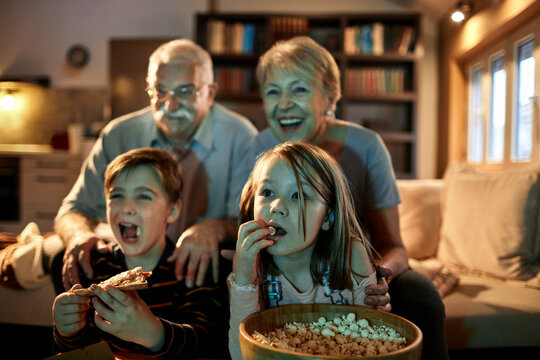 Grandparents and grandchildren watching a movie on the tv in the living room at home