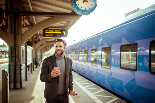 Young man using a smartphone while waiting for his train in a train station - Powered by Adobe