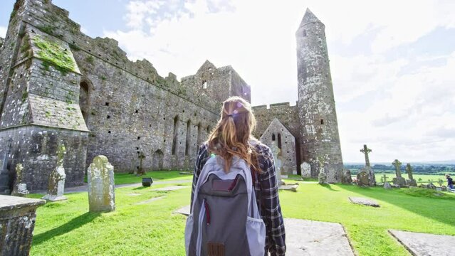 Woman with backpack walking through historical abbey in Ireland. Camera floating