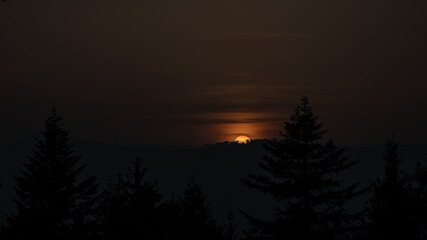 Sunset behind a hill with trees.