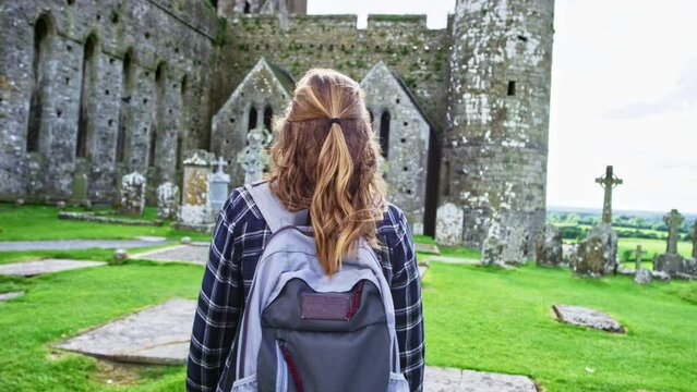 Woman walking towards Rock of Cashel castle. Adventure.