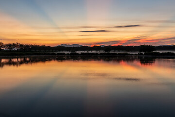 茨城県母子島遊水池の水面に映る朝焼けの筑波山と日の出の光芒