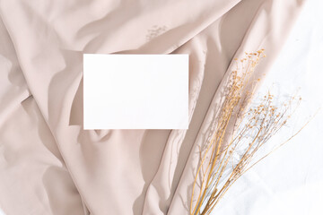 Minimalist square invitation card mockup on wavy white fabric with dried plants and window shadow background 