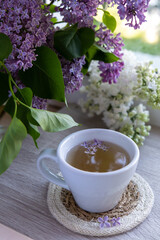Tasty black tea in white cup on windowsill with aromatic lilac flowers. Spring composition Cup of lilac tea drinking recipe flowering branches of purple lilac. Still life for copy space greeting card