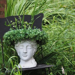 A stone statue of a woman's head with a wreath of leaves stands in a wild garden