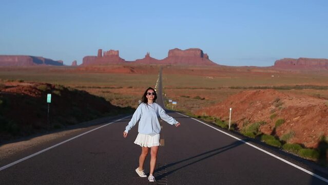 Happy young woman in white dress on the famous road to Monument Valley in Utah in her trip in USA. Amazing view of the Monument valley.
