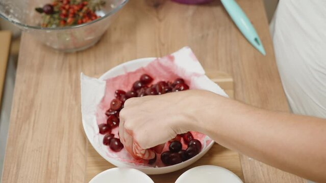 The woman is carefully removing the pits from the cherries using a knife in slow motion.