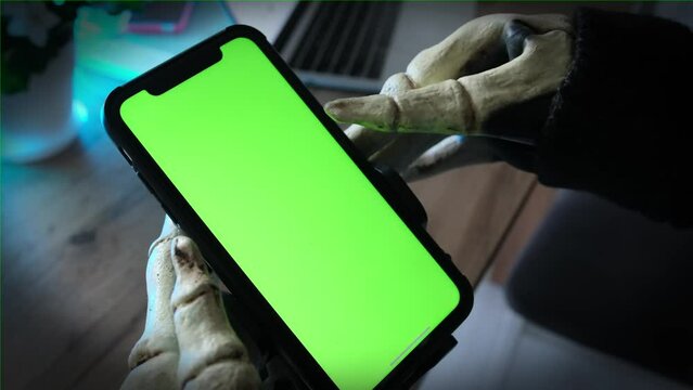 Hands in skeleton costume holding for smartphone with green screen. Dangers of communicating on social networks with strangers. Creepy Halloween party.
