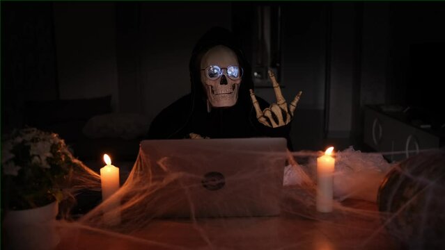 Spirit of death sitting on table laptop with cobwebs and lit candles, dark night, halloween celebration, technology and social media integral parts of modern-day celebrations. 