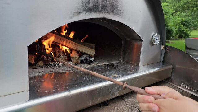 Outdoor metal pizza oven with person's hands stoking the flames
