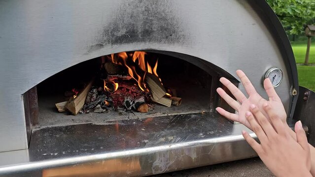Child warming hands by fire of outdoor pizza oven
