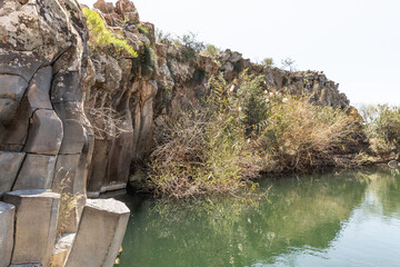 A small  lake with fish framed by hexagonal rocks with overgrown bushes and trees on the banks in Yehudia National Natural Park in northern Israel