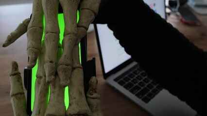 Bone hand maniacally stroking and hugging the phone with chromakey, night party invitation. Creepy Halloween party.
