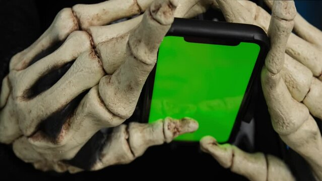 Hands in skeleton costume holding for smartphone with chromakey send message in chat, scrolls feed and leaves comments, close up. Halloween party, social media.