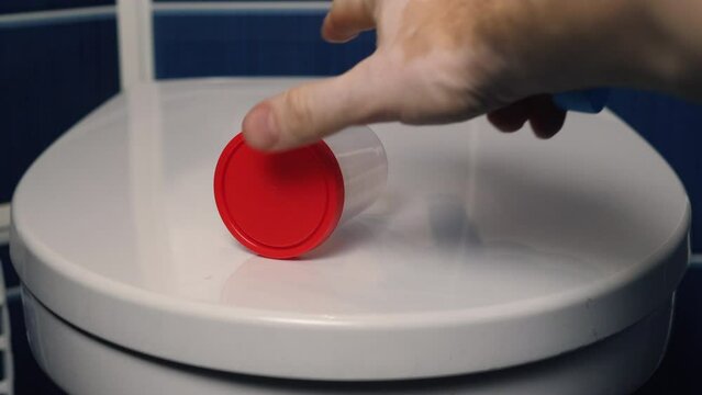 a man's hand takes containers for tests from the lid of the toilet bowl in the toilet. men's health care. the concept of medical tests, be healthy