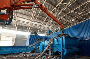 Grabbing excavator collects garbage in plant warehouse