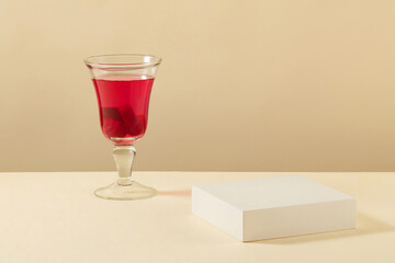 Background for the presentation of cosmetic products. On the beige background, an empty white podium decorated with glass of beetroot juice. Blank space for display mockup. Front view