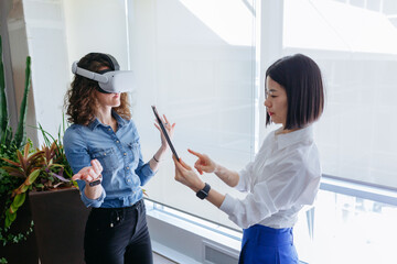 high angle view on two standing women in the office, one with VR and another with tablet