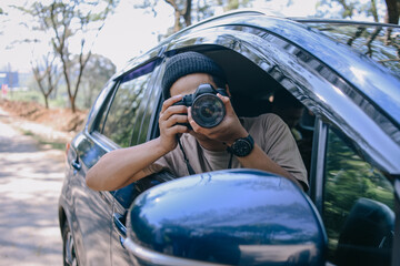 Young photographer man taking photos while sitting in a car. Male capturing a perfect view during road trip.