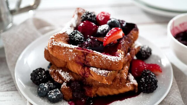 Eating freshly made french toast garnished with mix berry compote and powder sugar.