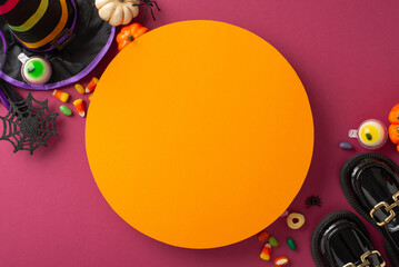 Dive into carnival fun with kid's Halloween ensemble. Top view of leather boots, enchanting hat, mystical wand, candy corn delights, pumpkins, spiders, on crimson backdrop with empty orange circle