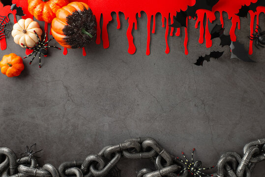 Arranging the Halloween ambiance. Top view photo featuring themed decoration setup: pumpkins, eerie spiders, spiderweb, bats, blood streaks, chain on textured concrete surface. Open space for text