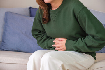 Closeup image of a sick woman suffering from stomachache, abdominal pain while sitting on sofa at...