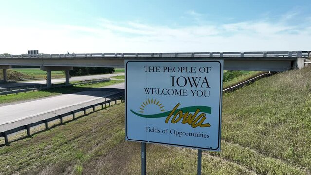 Welcome to Iowa state road sign. Aerial rising shot. Establishing shot as cars enter IA on interstate highway.