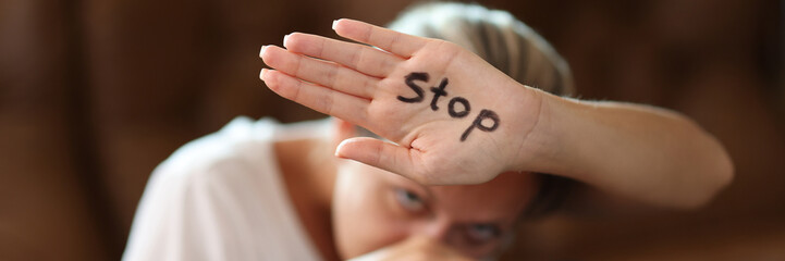Scared woman covering face with palm with stop inscription - obrazy, fototapety, plakaty